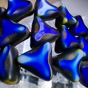 May include: A close-up of a group of blue and black glass triangle beads. The beads have a mottled, iridescent finish.