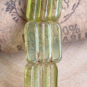 Puede incluir: Una hebra de cuentas de vidrio verde claro con textura acanalada. Las cuentas son de forma rectangular y tienen una apariencia translúcida.