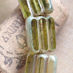 Può includere: Primo piano di una collana di perline di vetro verde con una finitura testurizzata e iridescente. Le perline sono di forma rettangolare e hanno una serie di linee orizzontali che le attraversano.