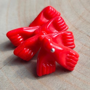 Könnte beinhalten: Eine Gruppe von fünf roten Plastikfüßen, jeder mit fünf Zehen, sind in einer Gruppe angeordnet. Die Füße sind alle in die gleiche Richtung ausgerichtet, und die Zehen zeigen alle nach außen. In der Mitte der Gruppe befindet sich eine kleine silberne Perle.