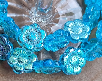 Puede incluir: Una hebra de cuentas de flores de vidrio azul turquesa. Las cuentas son iridiscentes y tienen un diseño de flor en relieve.
