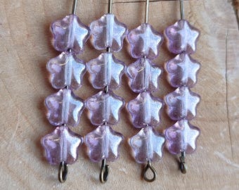 May include: A close-up of star-shaped beads in a grid. The translucent lavender beads have a subtle shimmer. Each bead is strung on a metal pin. The background is a light brown wooden surface.