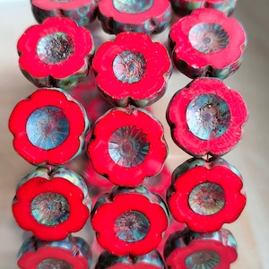 May include: A stack of red and blue flower-shaped beads with a metallic sheen. The beads are arranged in a circular pattern and have a raised center.