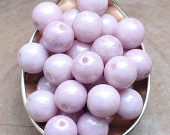 May include: A close-up of a silver spoon filled with pale pink, spherical beads. The beads have a speckled appearance and a matte finish. These beads are likely for crafting or jewellery making.