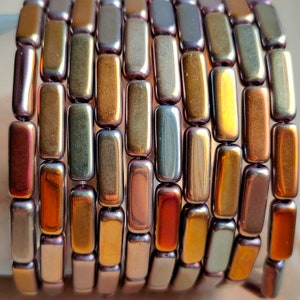 Könnte beinhalten: Nahaufnahme einer Reihe von regenbogenfarbenen Glasperlen. Die Perlen sind rechteckig und haben einen metallischen Glanz. Die Farben der Perlen sind eine Mischung aus Gold, Bronze und Lila.