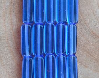 May include: A row of 18 blue glass beads with white stripes. The beads are rectangular in shape and have a glossy finish.
