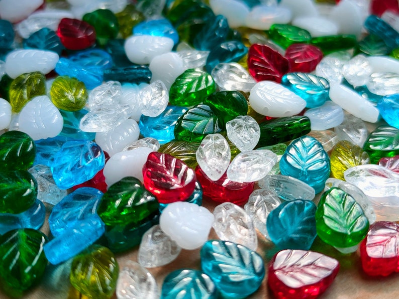 May include: Assortment of glass leaf-shaped beads in various colors, including clear, green, blue, and red. The beads are perfect for jewelry making or crafting projects.