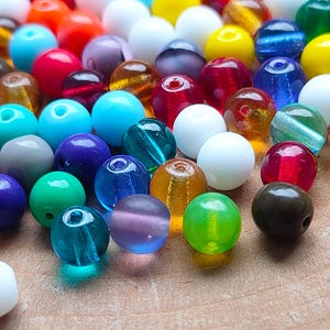 May include: A selection of colourful glass beads in various sizes and shades. The beads are a mix of opaque and translucent, with colours including red, blue, green, yellow, and white. Ideal for jewellery making and crafting.