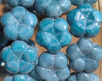 Puede incluir: Primer plano de varias cuentas de vidrio azules con forma de flor. Cada cuenta tiene una superficie texturizada y un diseño de cinco pétalos. Las cuentas están dispuestas en filas, creando un patrón visualmente atractivo. El color es una mezcla de turquesa y azul claro.