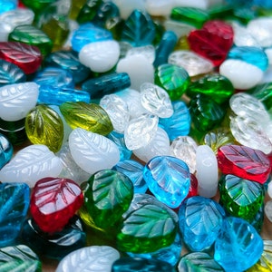 May include: Assortment of glass leaf beads in various colors, including white, green, blue, and red. The beads are all in the shape of a leaf and have a slightly textured surface.