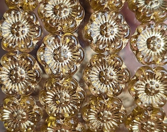 May include: A close-up of a string of gold-colored glass beads. Each bead is shaped like a flower with a raised center and multiple petals.