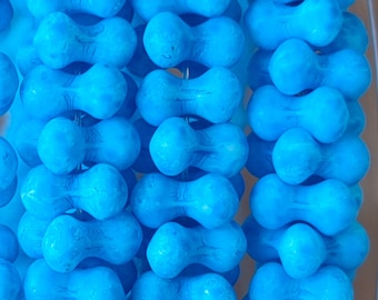 Puede incluir: Primer plano de una hebra de cuentas de color azul turquesa. Las cuentas tienen forma de cacahuete y un acabado liso y brillante.