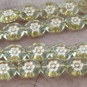 May include: A strand of light green glass beads with a flower design. The beads are faceted and have a gold-coloured flower design.