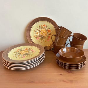 May include: A set of brown and yellow floral patterned dinnerware with a matching set of brown teacups and saucers.