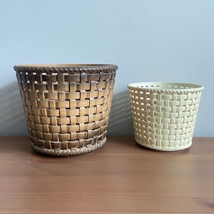 May include: Two woven plastic baskets, one brown and one cream, with a woven pattern. The baskets are on a wooden surface.