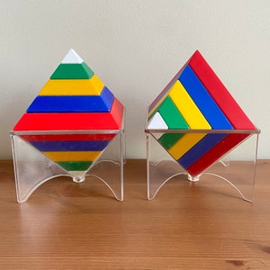 May include: Two colourful geometric pyramid puzzles made of plastic blocks. The pyramids are red, blue, yellow, and green. The pyramids are on clear plastic stands.