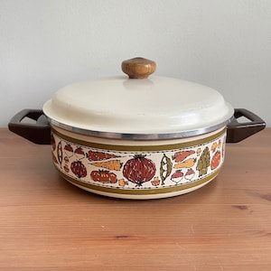 May include: Vintage white enamel pot with a brown and green vegetable design. The pot has a lid with a wooden knob.
