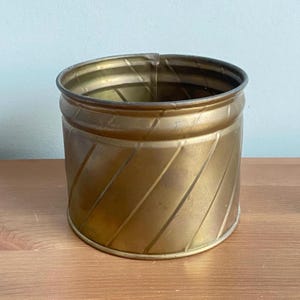 Peut inclure: Un pot de fleurs en métal doré avec un motif de nervures diagonales. Le pot est rond et a une finition lisse et brillante.