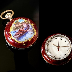 May include: Two antique pocket watches. One watch has a red enamel case with a painted scene and gold accents. The other watch has a white face with black numerals and gold hands, set in a red enamel case.