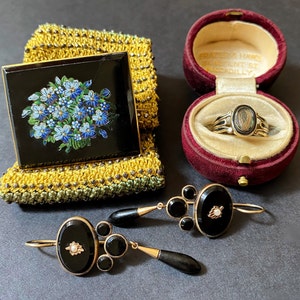 May include: A set of three antique jewelry pieces: a black enamel brooch with a floral design, a ring with a black cameo set in gold, and a pair of black onyx earrings with gold accents.