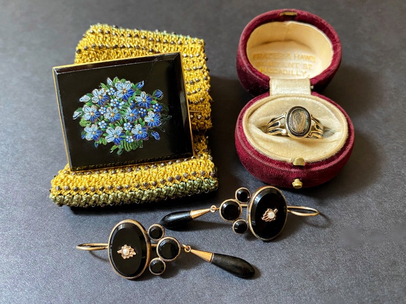 May include: A set of three antique jewelry pieces: a black enamel brooch with a floral design, a ring with a black cameo set in gold, and a pair of black onyx earrings with gold accents.