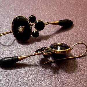 May include: A pair of antique earrings with black onyx and pearl accents. The earrings are made of gold and have a dangling design.