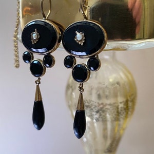 May include: A pair of antique black onyx drop earrings with gold accents and a pearl detail. The earrings feature a teardrop-shaped pendant and a cluster of round stones.