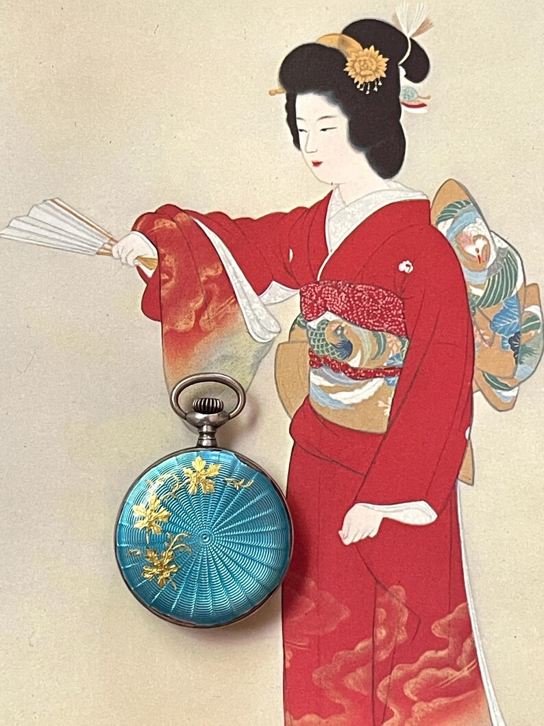 May include: A round pocket watch with a vibrant turquoise guilloch&eacute; enamel finish, featuring a delicate gold-toned floral overlay. The watch has a silver-colored metal casing and a circular winding crown at the top, showcasing intricate radial patterns.
