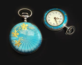 May include: Two round pocket watches with bright turquoise guilloché enamel cases. One watch shows a gold floral overlay on the back, while the other displays a white dial with black Arabic numerals and gold hands, featuring a turquoise enamel bezel.