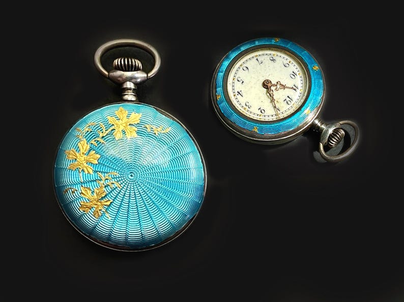 May include: Two round pocket watches with bright turquoise guilloch&eacute; enamel cases. One watch shows a gold floral overlay on the back, while the other displays a white dial with black Arabic numerals and gold hands, featuring a turquoise enamel bezel.