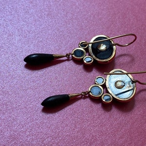 May include: A pair of gold earrings with black and white round stones. The earrings have a teardrop-shaped dangle with a black stone.
