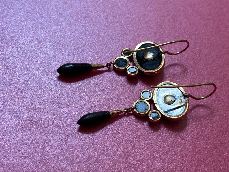 May include: A pair of gold earrings with black and white round stones. The earrings have a teardrop-shaped dangle with a black stone.
