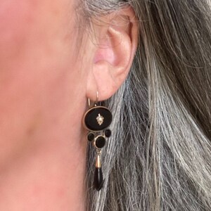 May include: A pair of dangle earrings with black onyx and a single diamond accent. The earrings are gold-toned and feature a teardrop-shaped onyx pendant.