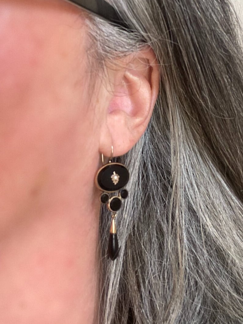 May include: A pair of dangle earrings with black onyx and a single diamond accent. The earrings are gold-toned and feature a teardrop-shaped onyx pendant.