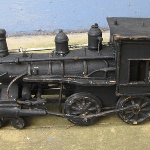 May include: A black wooden toy train engine with a caboose. The train has a detailed design with multiple wheels and a smokestack.