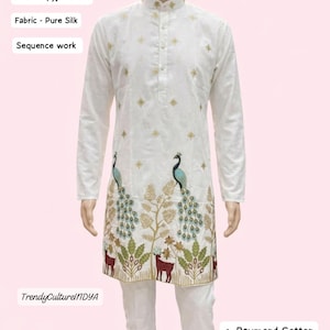 Könnte beinhalten: Weißes Kurta- und Pyjama-Set mit Sequenzarbeiten. Der reine Seidenstoff zeigt ein Pfauen- und Hirschdesign in Grün-, Blau- und Brauntönen. Erhältlich in den Größen M bis XXL.