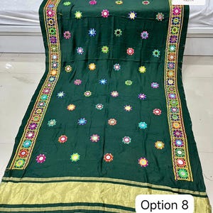 May include: A dark green textile with colorful embroidered accents and small mirrors. The edges feature a decorative border with intricate patterns and gold trim. The text "Option 8" is visible.