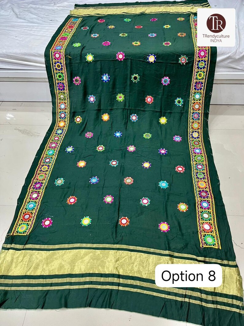 May include: A dark green textile with colorful embroidered accents and small mirrors. The edges feature a decorative border with intricate patterns and gold trim. The text "Option 8" is visible.