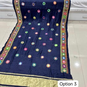 May include: Navy blue textile with colorful embroidered floral patterns and small mirrors. The edges feature a detailed border with geometric designs and gold accents. The textile has the text "Option 3" in a white box.
