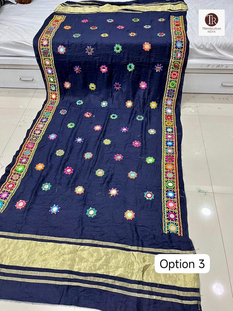 May include: Navy blue textile with colorful embroidered floral patterns and small mirrors. The edges feature a detailed border with geometric designs and gold accents. The textile has the text "Option 3" in a white box.