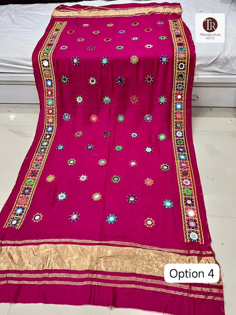 May include: A magenta textile with intricate embroidery and mirror work. The edges are adorned with colorful geometric patterns and small mirrors. The textile features numerous small, circular mirrors and the text "Option 4".