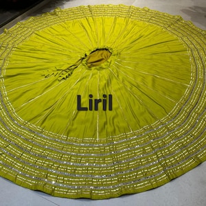 May include: A lime green skirt with a wide, circular design. The skirt features multiple rows of silver embellishments along the bottom edge. The word "Liril" is printed in black across the center of the skirt.