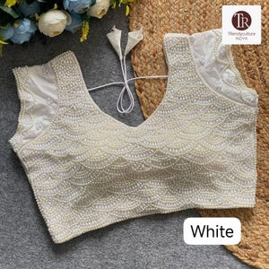 May include: A white, sleeveless top with a deep V-neck, adorned with numerous small, round, pearl-like beads. The beadwork creates a scalloped design across the front. The word "White" is displayed in a white rectangle at the bottom.