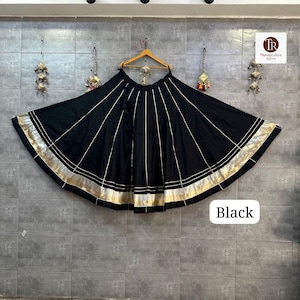 Puede incluir: Falda negra con ribete dorado y rayas doradas verticales. La falda está colgada de una percha de madera. La palabra "Black" está escrita en un recuadro blanco en la parte inferior de la imagen.