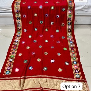May include: A vibrant red textile with intricate embroidery and mirror embellishments. The fabric features a repeating pattern of colorful circular designs and a decorative border. The text "Option 7" is visible in the lower right corner.