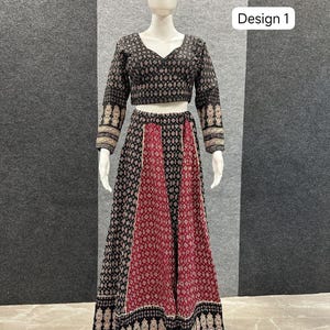 May include: A two-piece outfit on a mannequin. The top is a long-sleeved, black crop top with a V-neck and a repeating pattern. The skirt is a long, flowing skirt with a black and red pattern. The text "Design 1" is visible.