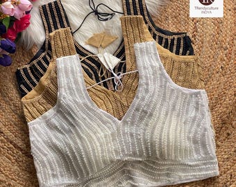 Può includere: Una collezione di tre camicette con scollo a V con perline in bianco, oro e nero. Le camicette sono impreziosite da file verticali di perline. Il testo "3 color options available" è in basso nell'immagine. Le camicette sono esposte su una superficie tessuta.