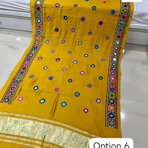 May include: Mustard yellow textile with intricate embroidery and mirror work. The fabric features a repeating pattern of colorful floral designs and a border with detailed stitching. The text "Option 6" is visible in the lower right corner.