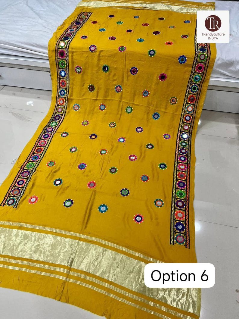 May include: Mustard yellow textile with intricate embroidery and mirror work. The fabric features a repeating pattern of colorful floral designs and a border with detailed stitching. The text "Option 6" is visible in the lower right corner.