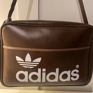 Sac Adidas, vintage des années 1970. Nouveau vieux stock.  Sac à bandoulière en vinyle marron foncé, avec logo blanc. Fabriqué en Yougoslavie.